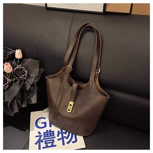 Detail of dark brown faux leather tote bag with golden twist lock on a black leather sofa