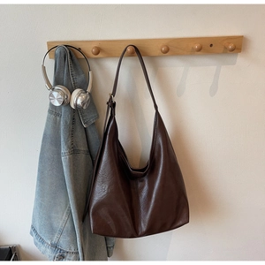 Close-up of vintage brown leather tote bag with natural texture hanging on a wooden hook