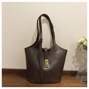 Detail of dark brown leather tote bag featuring a gold metal buckle on a wooden table