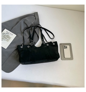 Detail of black suede messenger bag with silver metal eyelets and adjustable buckle strap