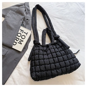 Détail du sac cabas matelassé noir avec bandoulière nouée sur un tissu blanc doux