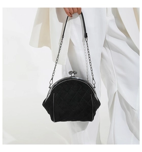 Detail of black quilted kiss-lock handbag with silver chain strap held by a model