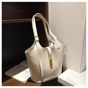 Detail of cream tote bag with wrinkled texture, gold buckle on a vintage bookshelf
