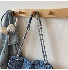 Gros plan du sac en jean matelassé bleu avec chaîne argentée sur un support en bois naturel