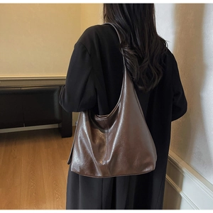 Detailed view of a dark brown glossy leather hobo bag worn by a model in a casual setting