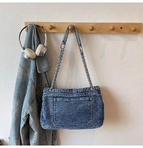 Détail du sac bandoulière en denim délavé avec chaîne en métal et poche apparente