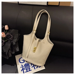 Detail of creamy white pleated leather tote bag with gold metal lock on black sofa