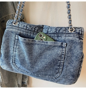 Détail du grand sac à bandoulière en jean montrant la poche extérieure et la bandoulière chaîne