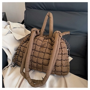 Détail du sac cabas matelassé marron avec cordon de serrage posé sur un siège en cuir