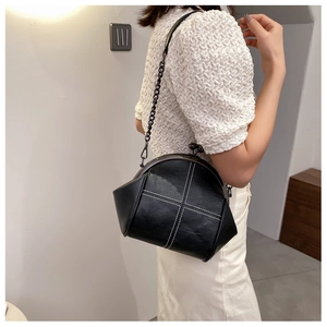 Detail of black shell bag with white cross-stitching and metal chain shoulder strap