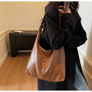 Close-up of a large brown leather shoulder bag with glossy texture and wide strap