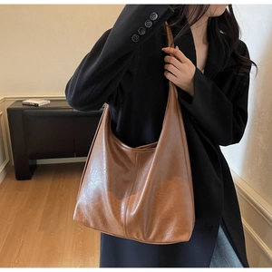 Close-up of a brown oversized soft leather tote bag worn by a model in a minimalist room