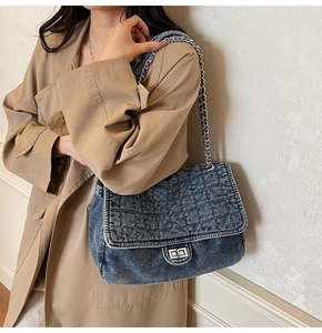 Detail of blue denim quilted handbag with silver chain strap and metal turn-lock closure