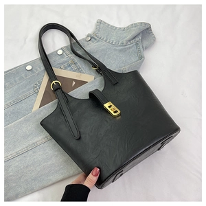 Detail view of large black tote bag with textured matte leather and golden metal buckle