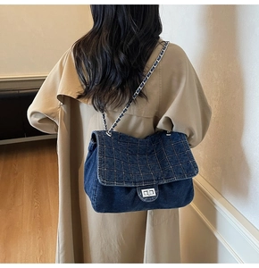 Detail of dark blue denim flap bag with quilted stitching and silver metal chain strap