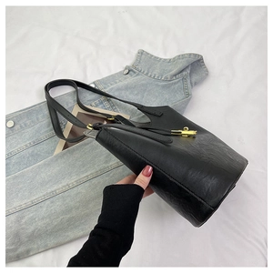 Detailed macro view of black textured leather bucket bag with elegant gold metal bar closure