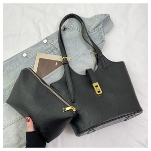 Flat lay of black faux leather tote bag and pouch set with golden metal twist lock detail