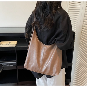 Detail of a large brown faux leather tote bag with vertical stitching and wide strap