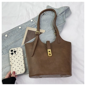 Detail view of brown faux leather tote bag with gold metal clasp and adjustable straps