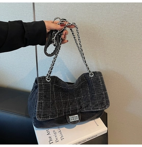 Detail view of black denim quilted bag featuring silver twist lock and metal chain strap