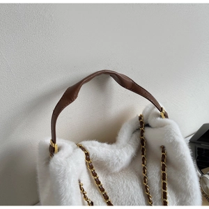 Detail of white faux fur tote bag featuring brown leather strap and gold chain link