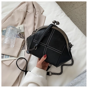 Detail of black shell-shaped crossbody bag with white contrast stitching and metal chain