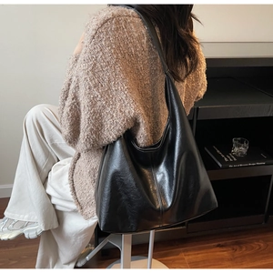 Detailed side view of a large black glossy Hobo tote bag with elegant pleated texture