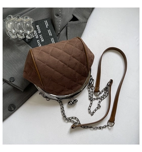 Detail view of brown quilted handbag with metal clasp and chain strap on grey blazer