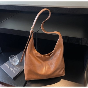 Detailed view of brown PU leather hobo bag texture and wide strap on a minimalist display