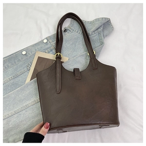 Detail of dark brown leather tote bag showing adjustable strap and golden buckle hardware