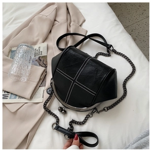 Close-up of black shell bag featuring white cross-stitch quilting and chain strap