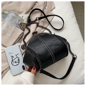 Detail of black leather shell bag featuring white cross-stitching and metal clasp closure
