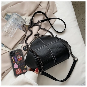 Detail of black leather shell bag featuring white cross-stitch and retro metal clasp