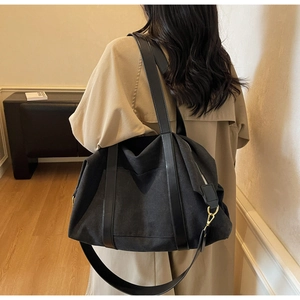 Detail view of large black canvas tote bag with leather straps on a model in a warm room