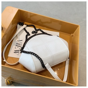 Detailed top view of white quilted shell bag with black metal clasp in warm amber setting