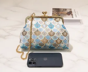 Detail of vintage floral embroidered handbag with chain strap shown next to a smartphone