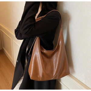 Deep brown oversized hobo bag in textured faux leather worn by a model in a black coat