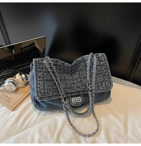 Macro detail of dark blue quilted denim texture and silver metal chain strap on handbag