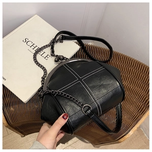 Close-up of black retro shell bag with white cross stitching and metal chain strap