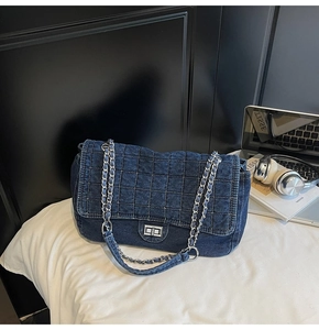 Detail of blue denim quilted handbag with silver chain and twist lock in lifestyle setting