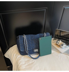 Detail of dark blue denim quilted shoulder bag with silver metal swivel lock on white bed