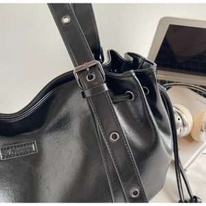 Détail d'un sac seau en PU noir brillant avec cordon de serrage sur un bureau