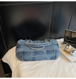 Close-up of vintage denim chain bag with quilted flap and metallic strap on white linen