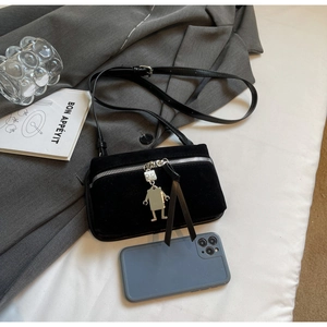 Detail view of black suede crossbody bag with robot charm on a grey blazer background