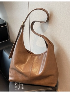 Large caramel leather tote bag with wide adjustable shoulder strap leaning on a wall