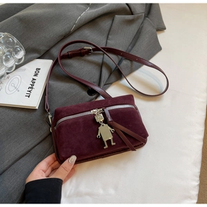 Close-up of burgundy suede bag featuring robot charm, metal zipper, and long tassels