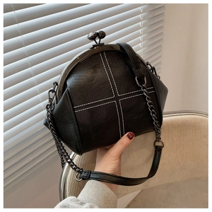 Detail view of the black shell bag with white cross stitching and retro metal clasp