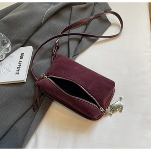 Detail of burgundy faux suede crossbody bag with metal charm and dual zipper