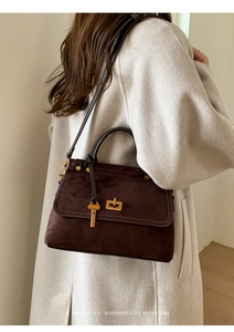Detail of dark brown matte suede handbag with gold buckle and key on ivory coat