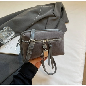 Detail view of grey suede texture crossbody bag featuring a silver robot pendant charm
